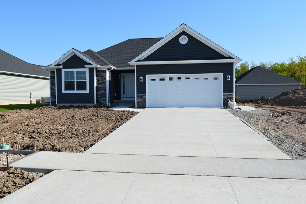 Fragment of brand new farmer's house with three garage doors and concrete driveway in front and blue sky background. Basketball ring in front of huge farmer's house.